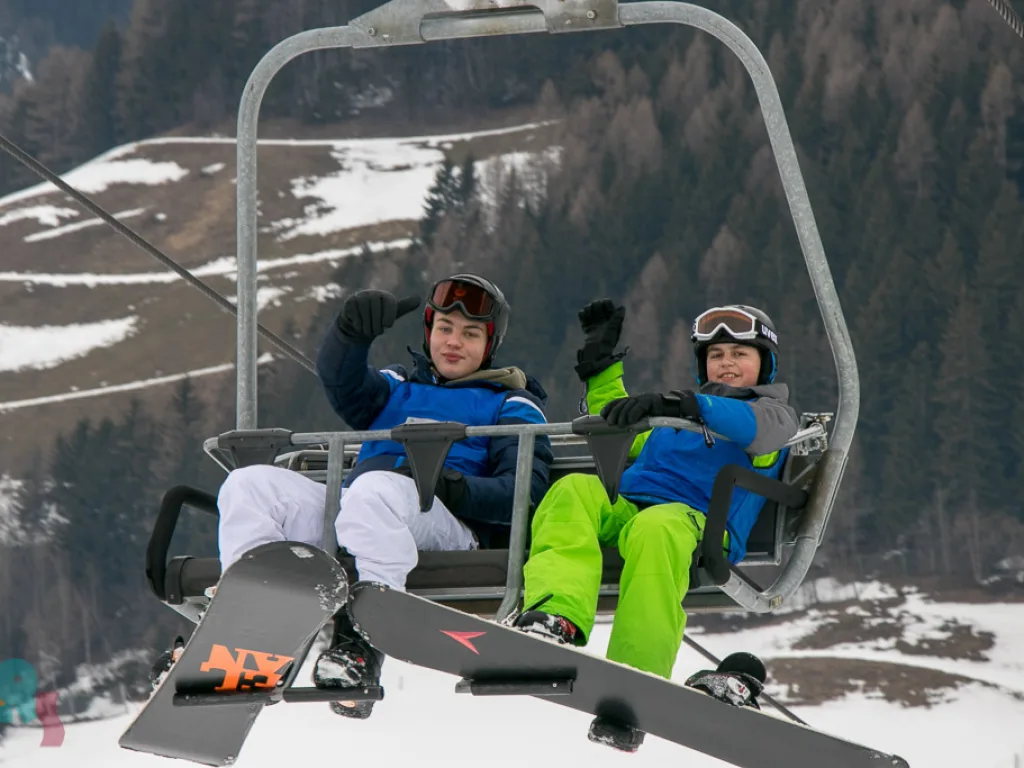 Zwei Jugendliche mit Snowboards im Sessellift.